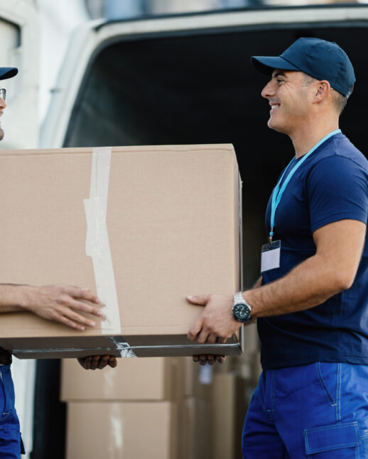 Happy manual worker cooperating while carrying cardboard boxes in a delivery van.